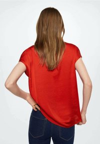 Blouse rouge à manches courtes en tissu léger et brillant avec une coupe décontractée. Le dos est plus long avec un ourlet arrondi.