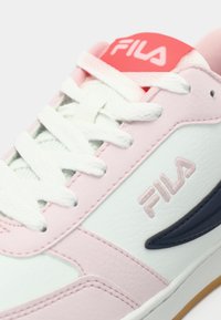 Λευκό και ροζ δερμάτινο αθλητικό παπούτσι με ανάγλυφες λεπτομέρειες, σχέδιο με κορδόνια, λογότυπο Fila στο πλάι και λαστιχένια σόλα. Διαθέτει επενδυμένη γλώσσα.