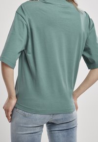 Tyrkysově zelené tričko s krátkým rukávem, volného střihu, s kulatým výstřihem a hladkou bavlněnou strukturou, doplněné o světle modré džíny.