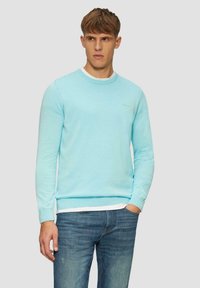 Hellblauer Pullover mit Rundhalsausschnitt, langen Ärmeln und gerippten Bündchen und Saum. Über einem weißen Hemd getragen, kombiniert mit blauen Jeans.