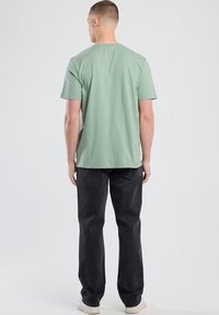 Light green short-sleeve t-shirt, cotton material, relaxed fit, paired with dark jeans. Simple design, no patterns or embellishments.
