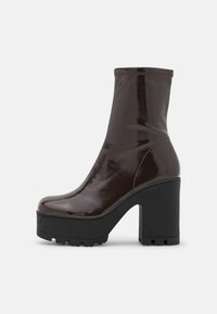 Bottine chelsea en simili cuir verni marron avec une finition lisse, un talon bloc haut et une semelle plateforme dotée d'un motif de semelle robuste.