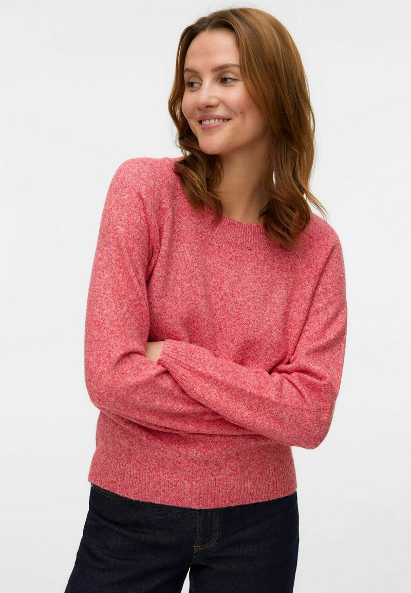 Pull en tricot texturé rose avec un col rond, des poignets et un ourlet côtelés. Accordé avec un jean foncé. Tissu doux de poids moyen.