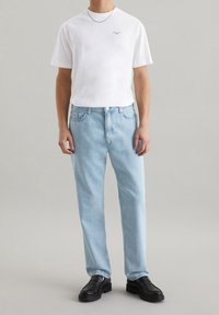 Maglietta bianca a maniche corte con un piccolo dettaglio stampato, abbinata a jeans in denim blu chiaro a gamba dritta. Mocassini neri completano l'outfit.