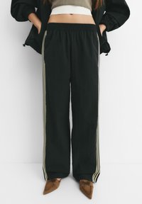 Pantaloni joggeri negri, lejeri, cu talie elastică și buzunare laterale, având dungi contrastante de un bej deschis pe lungimea picioarelor.
