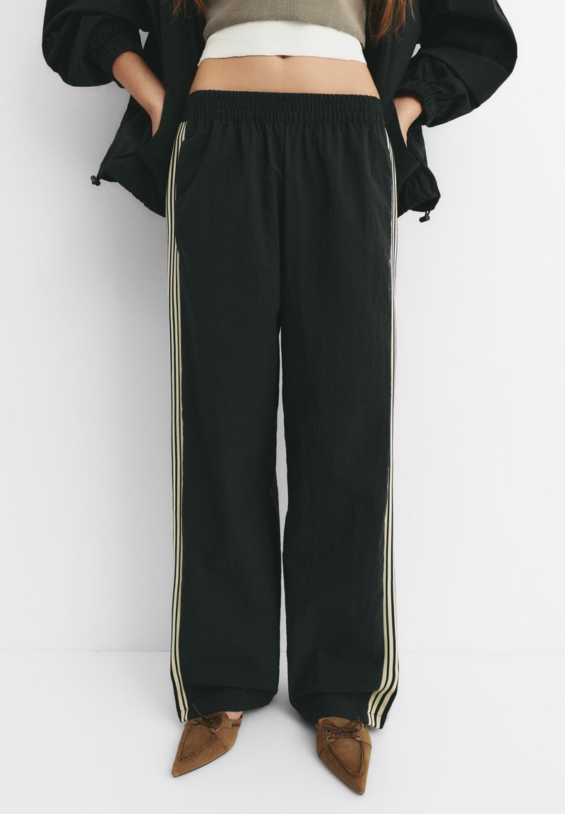 Pantaloni joggeri negri, lejeri, cu talie elastică și buzunare laterale, având dungi contrastante de un bej deschis pe lungimea picioarelor.