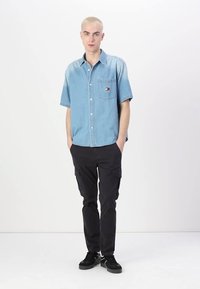 Ljust blå denimskjorta med kort ärm, ficka och logodetalj, tillsammans med svarta cargobyxor med sidofickor och avslappnad passform.