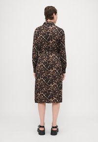 Rochie cu guler, de culoare neagră, cu un imprimeu animalier bej, maneci lungi, talie evidențiată printr-un brâu, lungime până la jumătatea gambei, asortată cu sandale groase negre.
