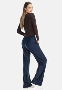 Brown long-sleeve top and navy wide-leg pants with side pockets, set against a plain white background. Model wearing white sneakers.