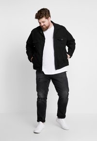 Black denim jacket with front pockets, button closure, and a collar; paired with a white t-shirt, dark distressed jeans, and white sneakers.