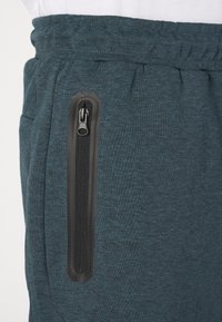 Teal joggers gemaakt van een zachte katoenmix, met een zijzak met rits en zwart metalen details, en een elastische tailleband voor comfort.