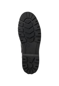 Semelle de chaussure en caoutchouc noir avec motifs de grip texturés et accents surélevés. Présente un logo circulaire et des motifs de semelles hexagonales variés.