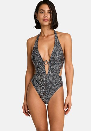 Femme portant un maillot de bain une pièce à col halter échancré avec un profond décolleté en V et un imprimé serpent, doté d'un détail en anneau au centre.