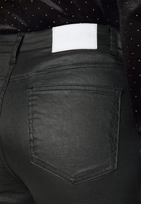Jeans de ganga pretos com uma textura suave, detalhes nos bolsos traseiros e uma etiqueta branca com texto em relevo "Glamorous Denim."