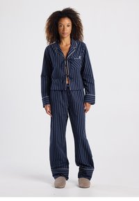 Navy striped pajama set featuring a tie-front jacket with a notched collar and matching pants with a loose fit and white accents.