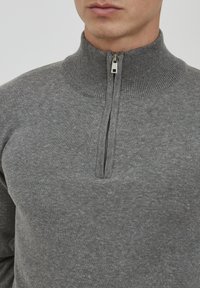 Maglione grigio con zip alta, realizzato in un morbido tessuto lavorato a maglia. Presenta una zip corta sul davanti e un colletto a coste testurizzate.