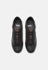 Baskets en cuir noir et tissu à motif marron avec lacets, offrant une texture lisse et un logo sur la semelle intérieure.