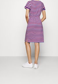 Robe rayée à manches courtes, arborant des rayures rouges, roses et bleues, taille cintrée et fente sur le côté. Associée à des baskets blanches.