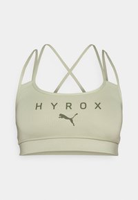 Svijetlo maslinasto zelena sportska grudnjak s križnim trakama, na kojem je ispisana riječ "HYROX" i Puma logo u tamnozelenoj boji. Glatka tekstura i rastezljiv materijal.