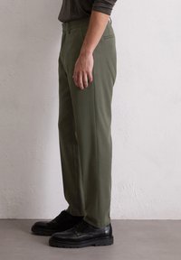 Pantalons vert olive au design droit, avec des poches latérales et une texture lisse, associés à des chaussures noires à lacets.