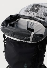 Rucsac negru cu un exterior texturat, căptușeală gri și închidere cu șnur. Interiorul prezintă o etichetă cu informații de urgență.