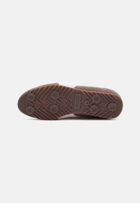 Sola de borracha castanha com um padrão em zig-zag, apresentando agarradores circulares. A parte superior é parcialmente texturizada e de cor clara, em contraste com a sola.