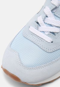 Gros plan sur la pointe d'une basket bleu clair avec des lacets blancs, une tige en mesh, des empiècements en daim et un bord de semelle en caoutchouc marron.