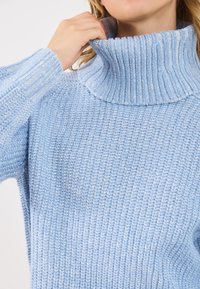 Ανοιχτό μπλε πλεκτό πουλόβερ με ψηλό γιακά και ραβδωτή υφή, διαθέτει μακριά μανίκια. Άνετη και ζεστή σχεδίαση.