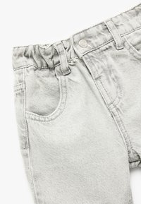 Lys grå denimbukser med elastisk talje, forlommer og bæltestropper. Struktureret stof med diskrete lodrette striber.