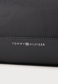 Black textured fabric wallet featuring a smooth leather trim, with white "TOMMY HILFIGER" branding printed on the front.