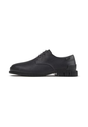 Zapato de vestir de cuero negro con suela gruesa ranurada y cordones, visto de lado sobre un fondo blanco.