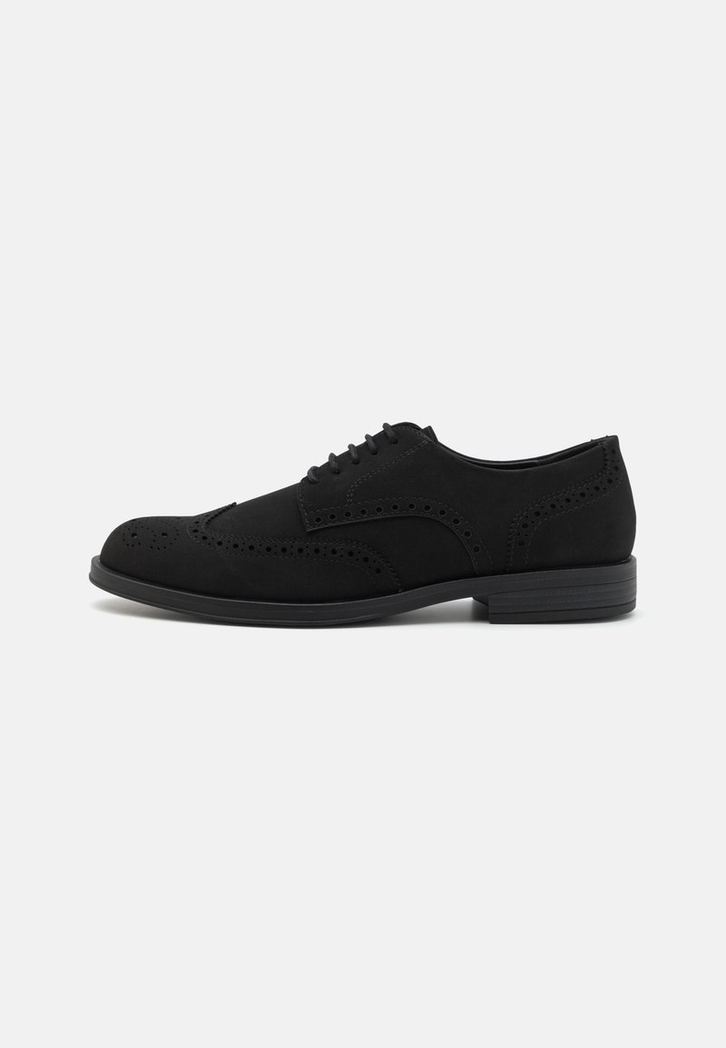 Chaussure Oxford en cuir noir à bout golf, avec des détails brogue et une fermeture à lacets, présentée sur un fond clair uni.