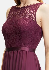 Bordeauxfarbenes Kleid mit einem Spitzenoberteil mit Blumenmustern, satiniertem Taillengürtel und fließendem Rock, das eine Mischung aus Texturen und satten Farben zeigt.