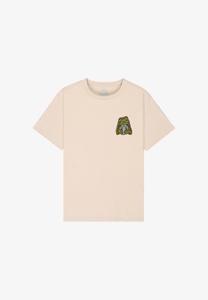 Beige T-shirt met korte mouwen en een kleine groene kikker die een cirkelvormig symbool vasthoudt, gedrukt op het linkerborstgebied.