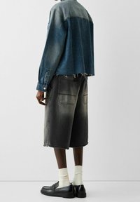 Giubbotto di jeans con una sfumatura blu, design corto; pantaloni shorts di jeans neri con effetto sbiadito; mocassini neri e calzini bianchi a 3/4.