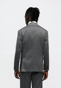 Hall halli ülikonajakk ruudulise mustriga, sälklapiga ja kahe nupuga. Kangal on sile tekstuur, näidatud tagantpoolt.