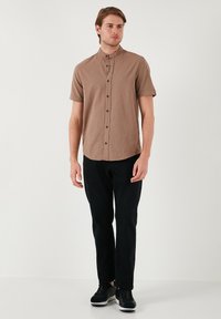 Korte mouwen bruine button-up shirt van textuurstof, gecombineerd met zwarte broek en zwarte sneakers.