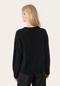Svart stickad tröja med ribbad rund halsringning och nederkant, med droppande axlar och en avslappnad passform. Mjuk textur, minimalistisk design.