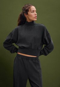 Felpa nera a maniche lunghe con collo alto, maniche oversize e orlo a coste, abbinata a pantaloni della tuta neri coordinati con vita elasticizzata.