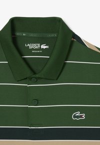 Polo shirt verde a righe con strisce orizzontali bianche, colletto a coste, due bottoni, logo Lacoste sul lato sinistro del petto, realizzato in tessuto liscio e traspirante.