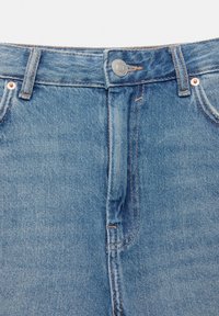 Svjetloplave traperice s visokim strukom, sadrže srebrne dugmadi, pet džepova i vidljive detalje šivanja.