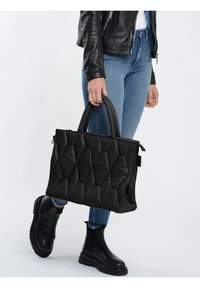 Sort quiltet håndtaske med en tekstureret overflade, dobbelte håndtag og lynlåslukning. Kombination med blå jeans og sorte ankelstøvler.