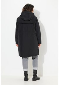 Zwarte waterdichte parka met een capuchon, middellange ontwerp, verstelbare taille en textiele stof. Beschikt over zijzakken en een rugventilatie.