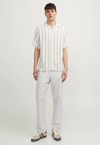 Kortärmad, randig skjorta med knappar i vitt med blå och lila ränder; kombinerad med ljusa byxor och beige sneakers.