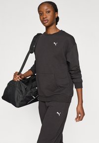 Μαύρο φούτερ με στρογγυλή λαιμόκοψη, ριμπ μανσέτες και τσέπη καγκουρό. Διαθέτει λευκό λογότυπο Puma στο στήθος. Συνδυάζεται με μαύρο παντελόνι και τσάντα.