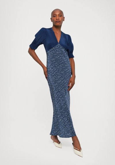 Navyblauwe jurk met korte pofmouwen; bedekt met witte stippen. Slim fit en vloerlengte, gemaakt van een gladde stof, met een diepe V-hals.