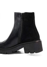 Black boot featuring a combination of smooth leather and suede, side zip closure, chunky rubber sole with tread pattern, and a solid heel.