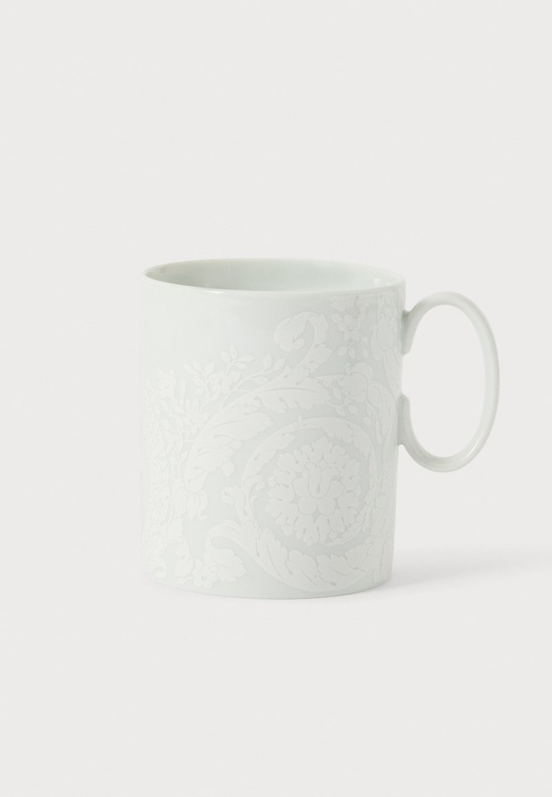 Tasse en céramique blanche avec un motif floral et feuillu en relief et une anse arrondie sur fond blanc.