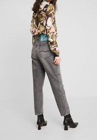 Blusa de gasa con estampado floral en verdes, rosas y blancos; combinada con unos jeans de mezclilla gris de tiro alto. Botines negros de tacón completan el look.