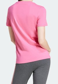 Pink short-sleeve t-shirt, crew neck, made of cotton, smooth texture, with a relaxed fit, paired with gray stretchy pants featuring pink side stripes.